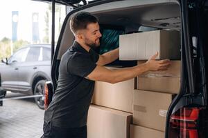Holding the packed product in hands., Delivery man or loader is near the car with a box photo