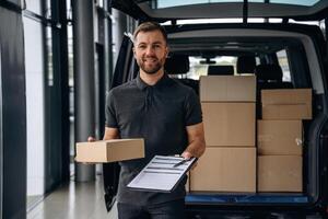 Pen and the notepad ,,in ,hands. Delivery man or loader is near the car with a box photo