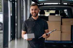 Business of delivery, with notepad., Man loader is near the car with a box photo