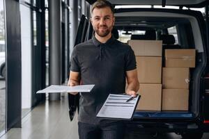 Pen and the ,notepad ,in ,hands. Delivery man or loader is near the car with a box photo