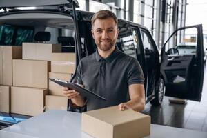 Business ,,of delivery, with notepad. Man, loader is near the car with a box photo