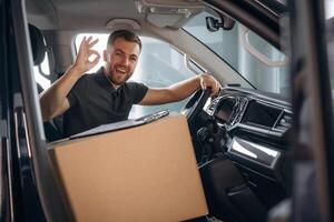 Showing, hand gesture, everything is fine, will be done. The delivery man or a loader is in the car with box photo