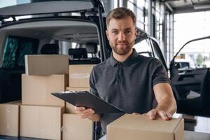 Positive facial expression,,, holding notepad. Delivery man or loader is near the car with a box photo