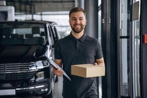 Standing, holding ,notepad. Delivery ,man or loader is near the car with a box photo