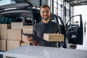 Business of delivery, ,,,with ,notepad. Man ,loader is near the car with a box photo