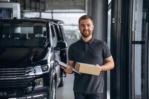 Front view, standing. Delivery,,, man or loader is near the car with a box photo