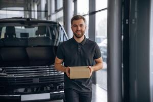Here's your delivery. Man ,,,loader is near the car with a box photo