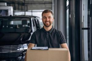 Smiling, positive facial ,,expression. Delivery man or loader is near the car with a box photo