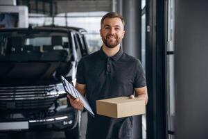 Standing, holding notepad... Delivery,, man or loader is near the car with a box photo