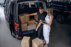 Woman, is helping delivery man ,,with ,products, holding notepad, loader is working with boxes from automobile photo