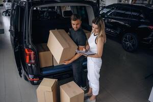 Woman is, helping, delivery man with products, holding notepad, loader is working with boxes from automobile photo