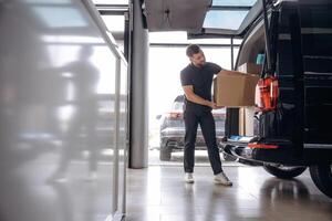 Holding the packed product ,,,in hands. Delivery man or loader is near the car with a box photo