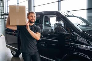 Big ,,order, holding the box. Delivery man or loader is near the car with photo