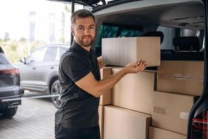 Holding ,the, packed product in hands. Delivery man or loader is near the car with a box photo