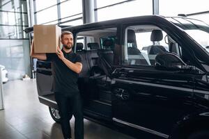 Big ,order, holding ,the box. Delivery man or loader is near the car with photo