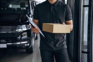 Front view, standing., Delivery, man ,or loader is near the car with a box photo