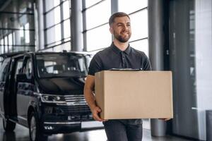 With, a ,box,, smiling. Delivery man or loader is near the car photo