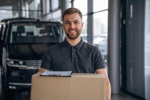 Smiling, ,positive facial, expression. Delivery man or loader is near the car with a box photo