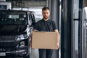 Front view, standing... Delivery man or loader is near the car with a box photo