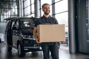 With ,a ,box, smiling. Delivery man or loader is near the car photo