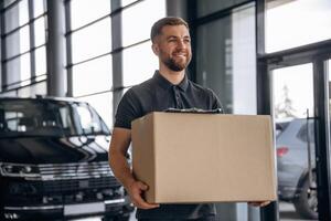 With a, box, smiling. Delivery man or loader is near the car photo