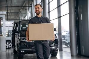 With a ,box,, smiling. Delivery man or loader is near the car photo