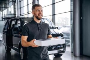 Delivery, man, or loader is near the car with a box photo