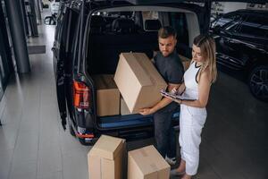 Woman, is helping delivery man with products, holding notepad, loader is working with boxes from automobile photo