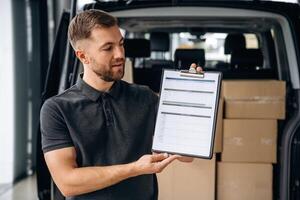 Confirm ,the ,order on notepad. Delivery man or loader is near the car with a box photo