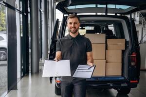 Pen ,and the notepad in hands. Delivery man or loader is near the car with a box photo