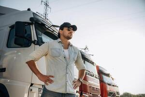 In the ,hat, standing. Truck ,driver is near the transport outdoors photo