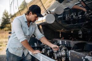 In, shirt ,and in a, cap. Truck driver is near the transport outdoors photo