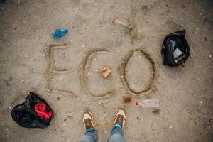 Top view of sand with word eco, trash on the ground, legs of the person photo