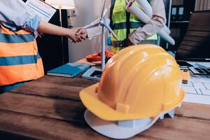 Two people shaking hands with a hard hat on a table photo