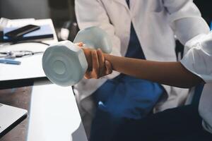 A doctor is holding a dumbbell while a woman is sitting at a desk photo