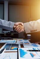 Business people shaking hands over a table with graphs and charts photo