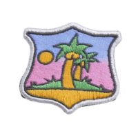 This shows embroidered patch featuring tropical scene with palm trees, sun, and colorful background. patch has shield shape with silver border.tropical patch with palm trees and sun png