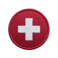 Round embroidered patch features white cross on red background, symbolizing first aid or medical emblem. design is simple and iconic, often associated with emergency services png