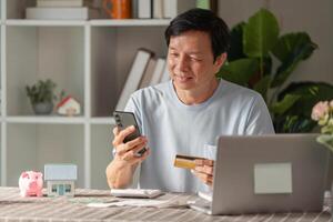 Senior man enjoying online shopping with a credit card and smartphone at home workspace photo