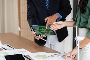 ESG Analysis and Collaboration. Team reviewing sustainability metrics on a tablet in office. photo