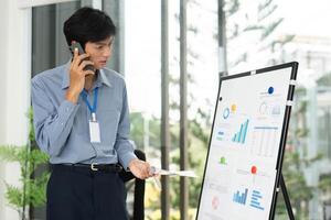 Business Presentation and Analysis. Professional man discussing data on a whiteboard while on a phone call. photo