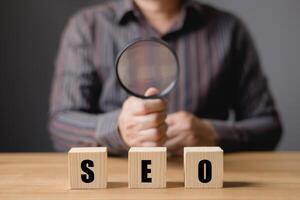 Businessman sit and holding magnifying glass.Searching Browsing Internet Data Information with wood block. Search Engine Optimization SEO Networking Concept. photo