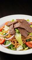 a plate of beef and noodles with tomatoes and lettuce photo