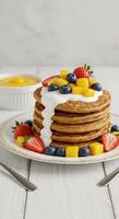 Delicious Pancakes Stack with Mango Strawberries Blueberries and Cream for Breakfast photo