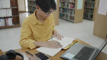 College student writing notes in library with laptop computer for homework, research, e-learning, project planning, literature reading and online study. video