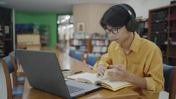 A young man studying and working on a laptop in the library while reading a book. video