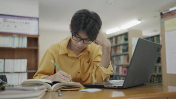 University student using laptop and writing notes in campus library for online learning. video