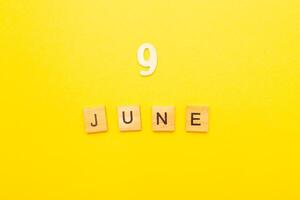 Top view of word 9 June calendar date made by wooden cubes on yellow color background photo