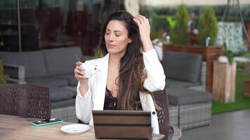 A woman is enjoying her coffee while actively working on her tablet in an outdoor setting video