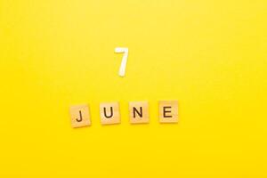 Top view of word 7 June calendar date made by wooden cubes on yellow color background photo